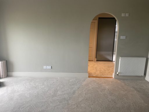 View of a large room with a grey carpet looking towards an archway through into another room.